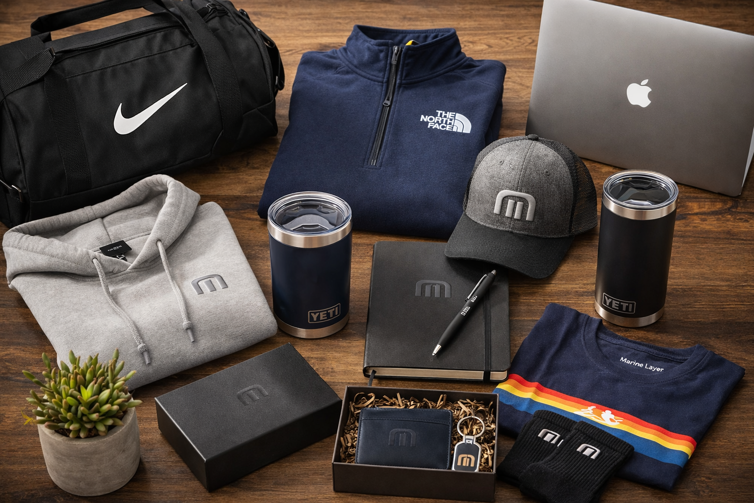 Premium corporate swag items including Nike duffel bag, YETI tumbler, branded apparel, and laptop arranged on desk for employee gifting and recognition programs
