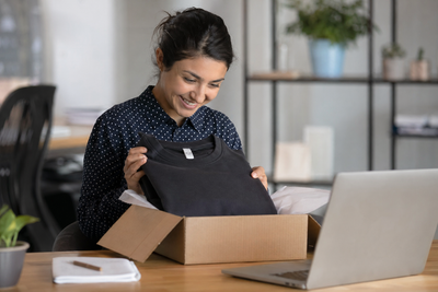 Employee opening a work anniversary swag package at desk with on-demand branded apparel, showcasing zero inventory company store and no minimum order program