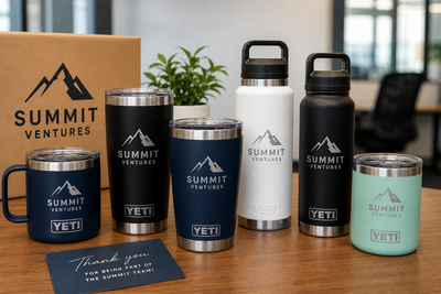 Branded YETI tumblers and premium insulated drinkware for corporate gifting displayed on an office desk, featuring custom logo engraving and on-demand company swag options for employees and clients in 2026